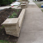A stone retaining wall running along a concrete sidewalk
