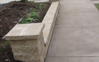 A stone retaining wall running along a concrete sidewalk